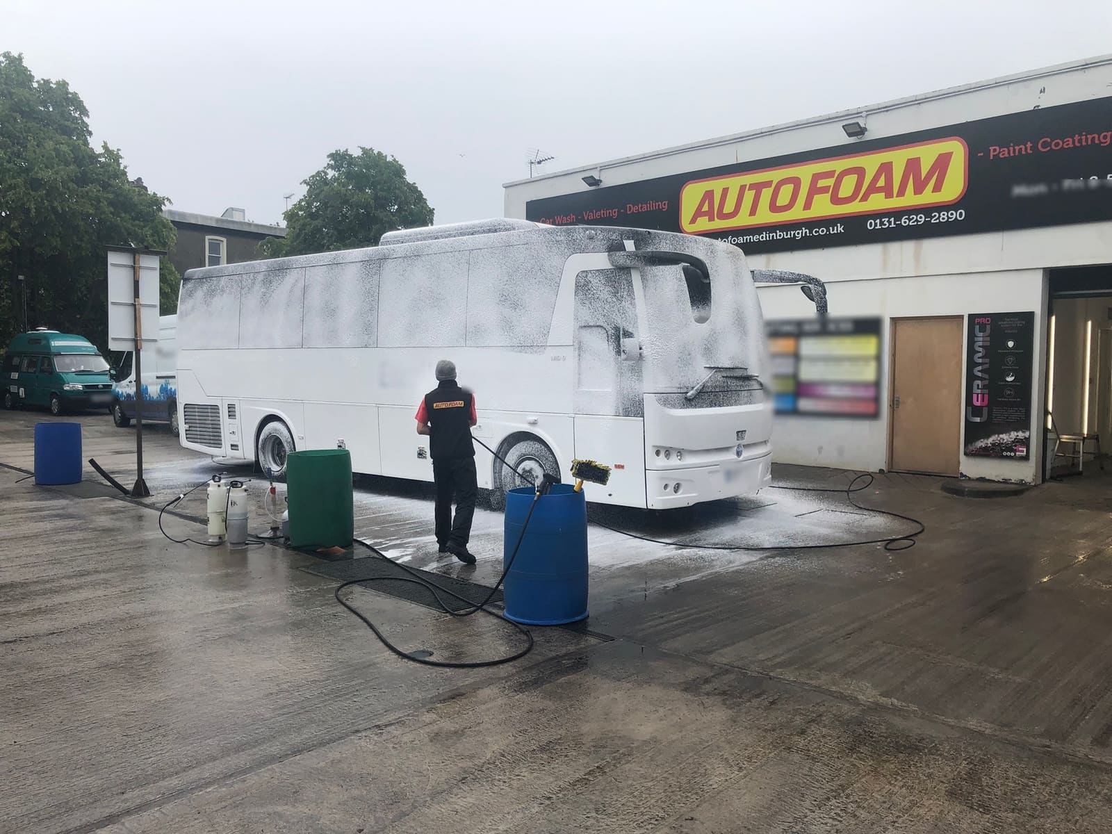 An Autofoam team member foam-washing a white coach on the forecourt