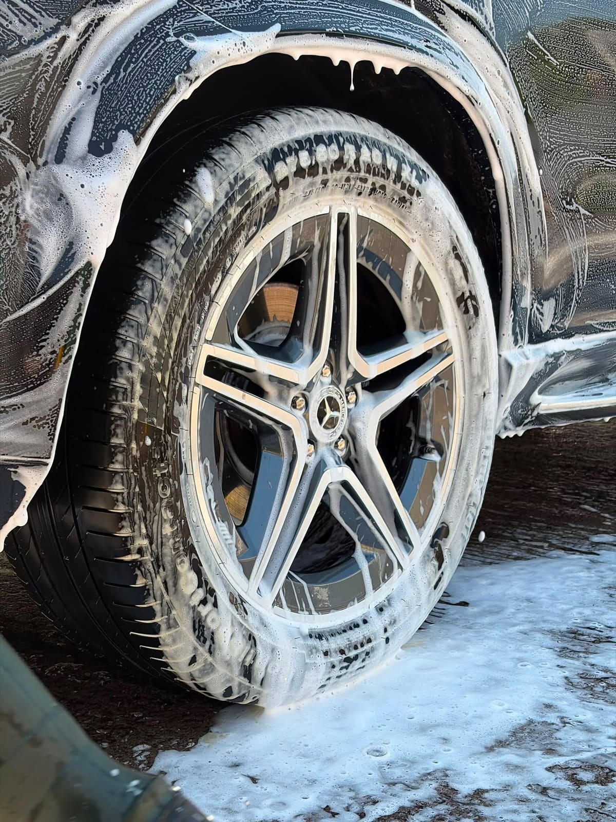 A Mercedes alloy wheel and tyre under snow foam