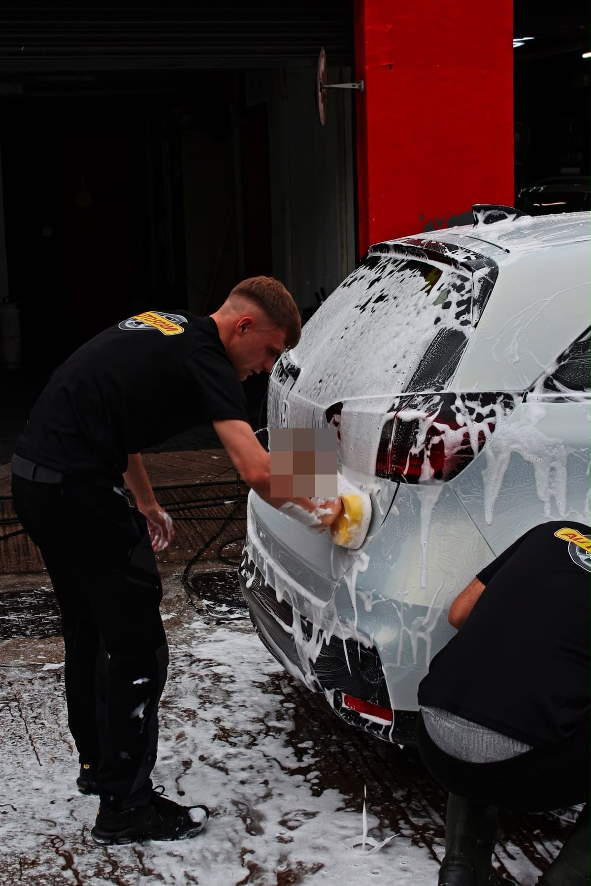 Two of the team hand-washing the back of a foam-covered BMW