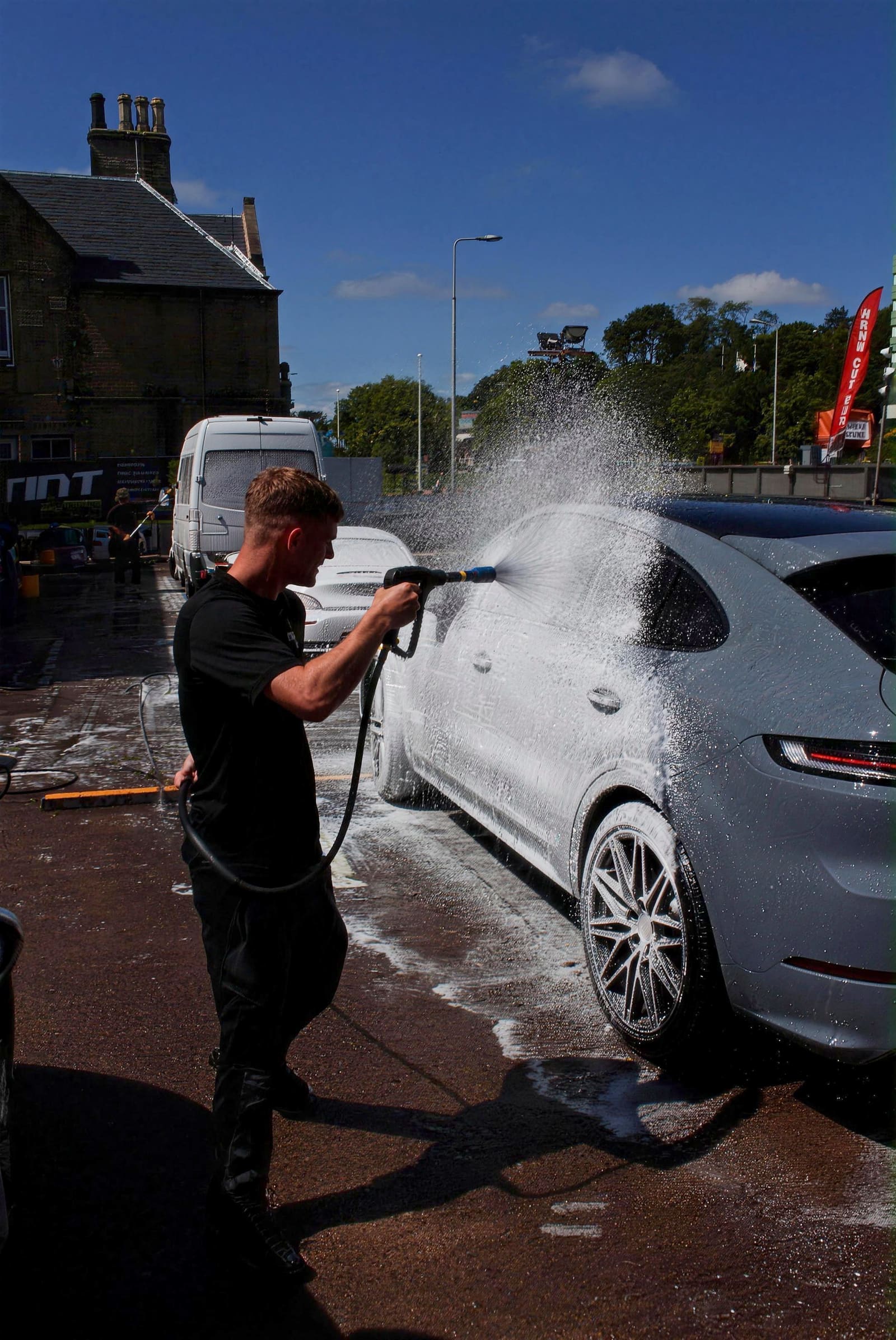 An Autofoam team member jet-washing a grey Porsche in the sunshine