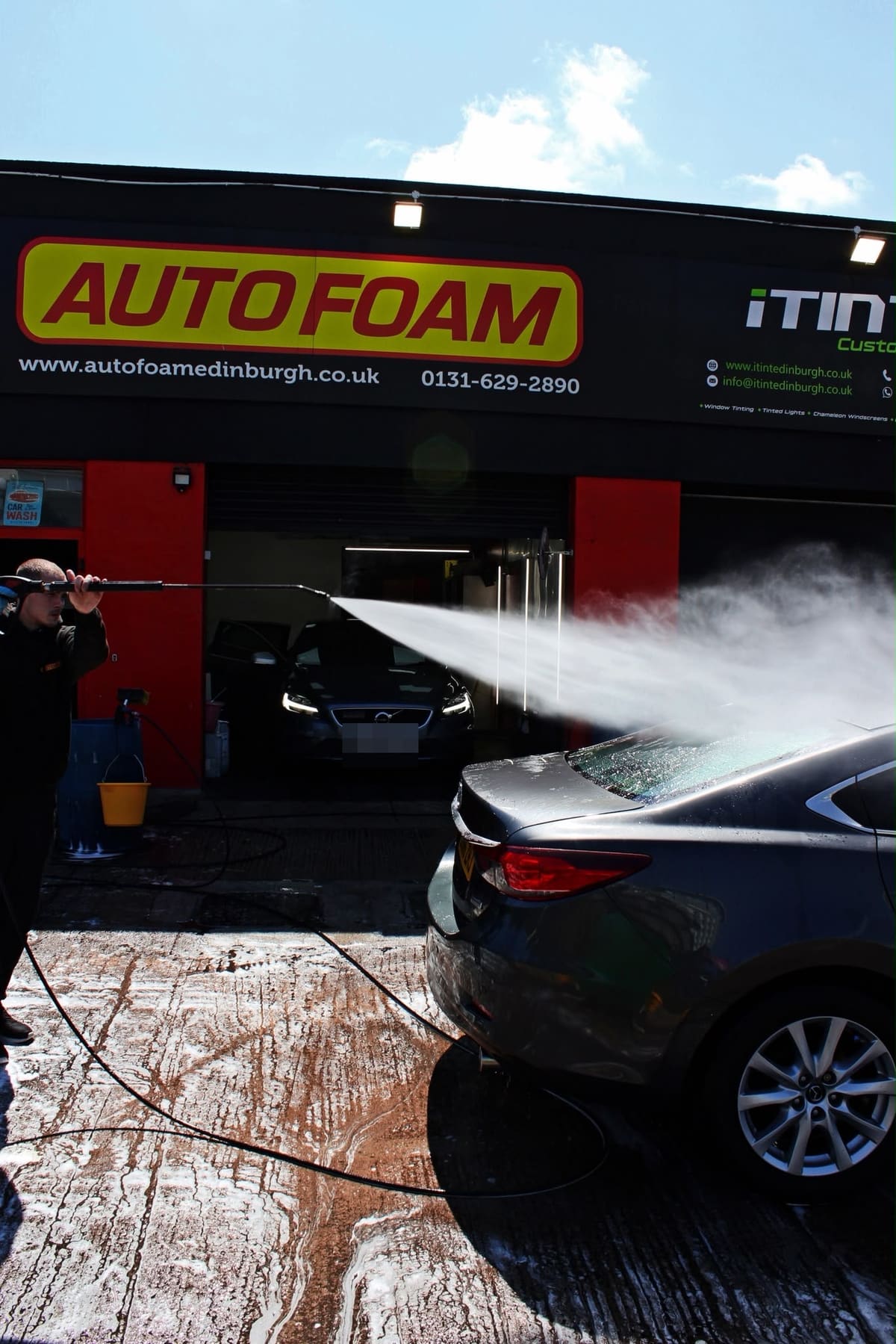 Jet-washing a car on the forecourt in front of the Autofoam shop sign
