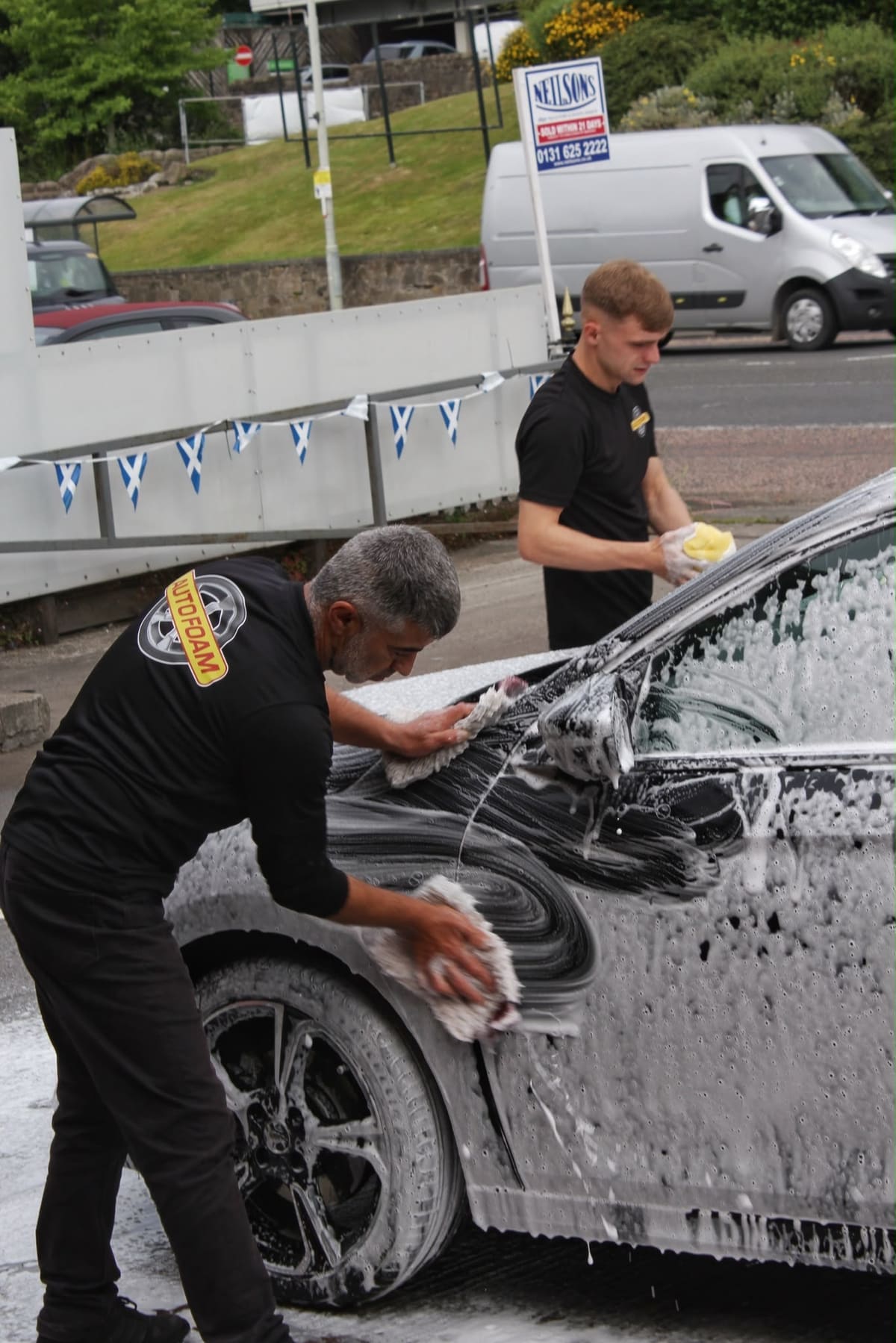 Two of the team hand-washing a black car on the forecourt