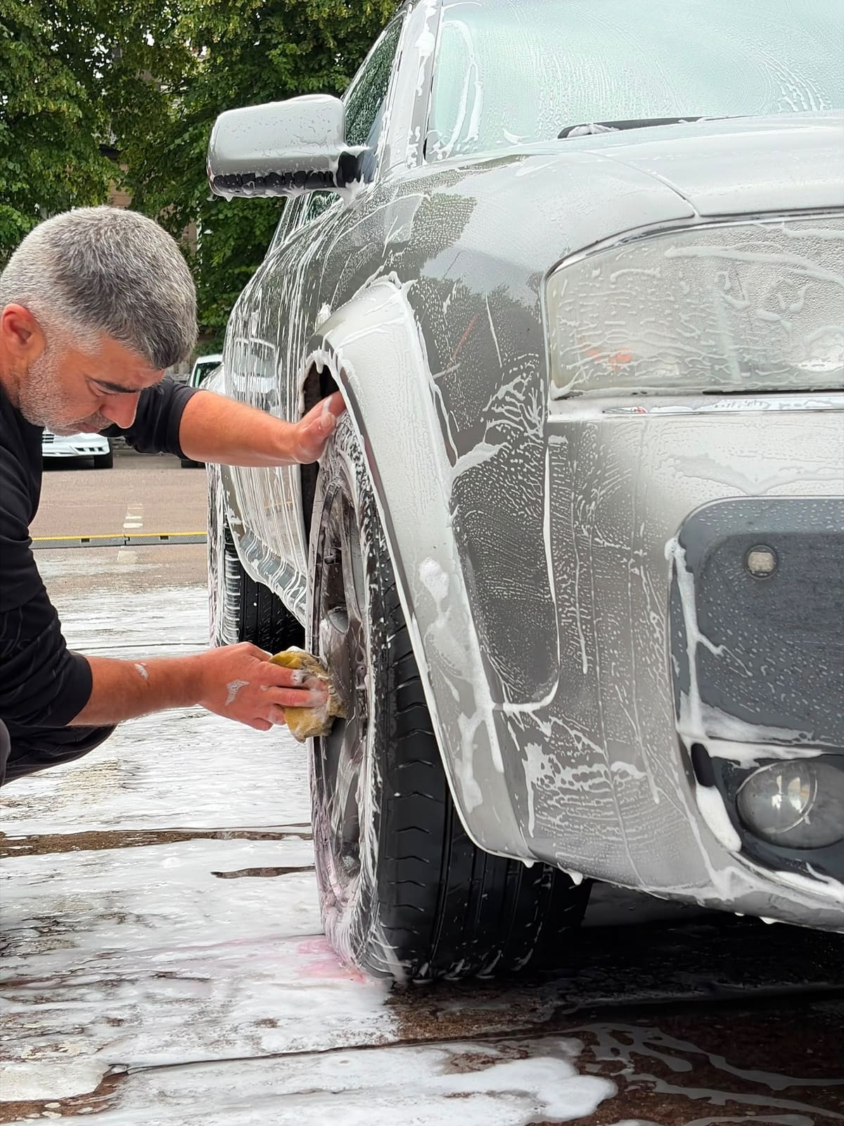 Scrubbing the wheel of a grey 4x4 by hand